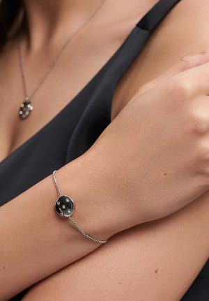 Silver-toned bracelet featuring a round, clear pendant with three small stones, secured with a thin, textured chain.