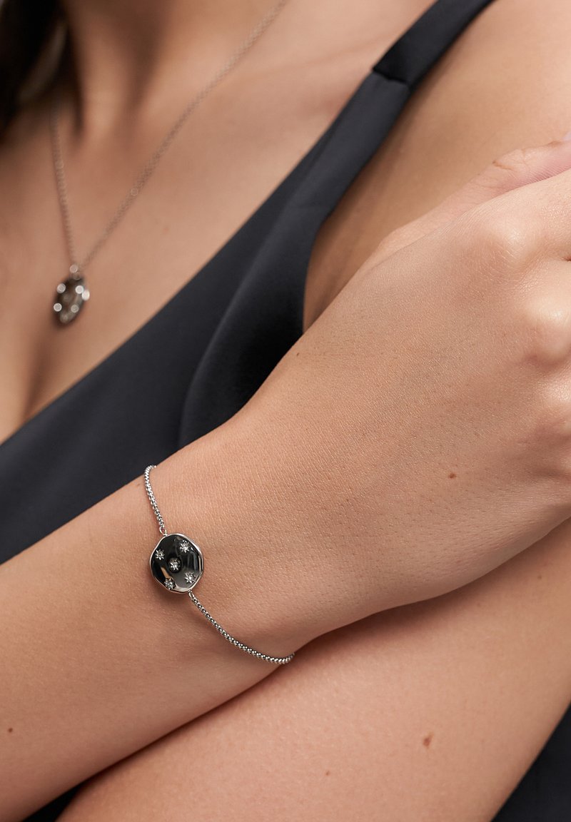 Bracciale in tono argento con un pendente rotondo e trasparente, impreziosito da tre piccole pietre, fissato con una sottile catena testurizzata.