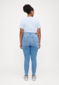 Camiseta azul claro, jeans de mezclilla de tiro alto en lavado medio con bolsillos traseros. Zapatillas plateadas en los pies, cabello rizado recogido. Diseño sencillo.