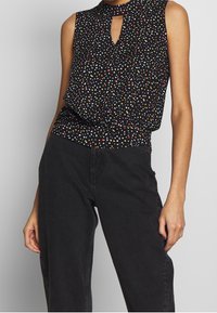 Top nero senza maniche con scollatura a chiave e pois multicolori, caratterizzato da una vestibilità comoda e una vita arricciata.