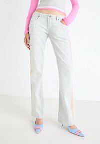Jeans acampanados de color gris claro con paneles laterales en un material texturizado rosa. Combinados con tacones azul con punta afilada y acentos rosas.