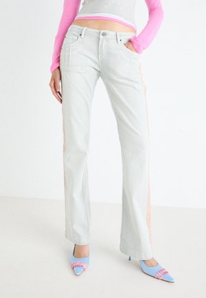 Light gray flared jeans featuring side panels in a textured pink material. Paired with blue pointed-toe heels with pink accents.