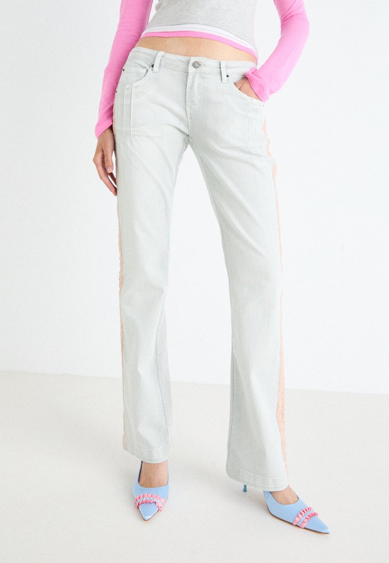 Jeans acampanados de color gris claro con paneles laterales en un material texturizado rosa. Combinados con tacones azul con punta afilada y acentos rosas.