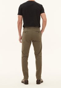 Chino verde oliva da uomo con vestibilità slim, dotato di due tasche posteriori e una texture liscia. Abbinato a una t-shirt nera e scarpe scure.