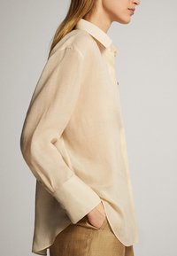 Beige, genomskinlig skjorta med knappar och spetsig krage samt långa ärmar. Har en loose fit och mjukt, texturerat tyg.