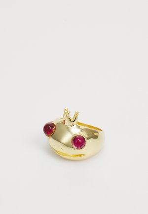 Anel de sapo dourado com uma coroa, apresentando realces redondos vermelhos para os olhos, uma textura lisa e uma forma arredondada.