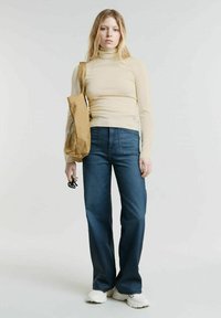 Maglione beige a maniche lunghe con collo a bottleneck, jeans flare blu scuro, sneakers crema e una borsa a tracolla marrone. La texture è liscia con una vestibilità strutturata.