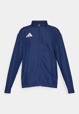 Chaqueta azul marino con cremallera, hecha de tela suave, con cuello alto, puños elásticos y logo de tres rayas blancas en el pecho izquierdo.