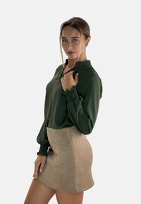 Green long-sleeve blouse with a high collar and gathered cuffs paired with a beige suede mini skirt featuring a side zipper.