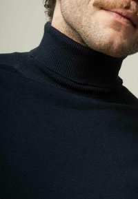 Navyblauwe geribbelde coltrui met een hoge kraag, zachte textuur en een aansluitend ontwerp, waarmee het nek- en schoudergebied wordt benadrukt.
