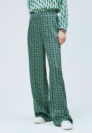 Pantalons larges à motifs verts avec un design floral, une taille haute et un tissu doux. Associés à des baskets blanches.