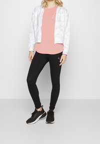 Light purple tie-dye zip-up hoodie, peach t-shirt, black leggings, black sneakers with white soles. Features logo on hoodie and leggings.