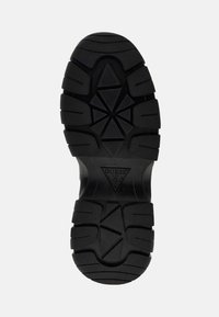 Semelle de chaussure en caoutchouc noir avec une surface texturée et décorée de motifs, comprenant des grips en forme de triangles et de rectangles ; logo embossé au centre.