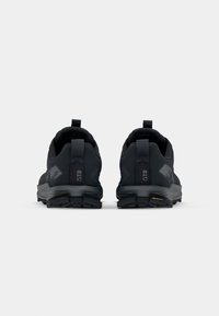 Baskets de sport noires avec un dessus texturé, un talon renforcé et une semelle en caoutchouc. Présente des languettes de traction et des accents de logo à l'arrière.