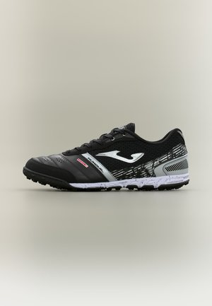 Scarpa sportiva nera e grigia con logo bianco, suola testurizzata e lacci, progettata per uso sportivo su erba sintetica o all'aperto.