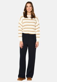 Striped sweater in cream and gold yarn, paired with navy wide-leg trousers and brown suede boots. Soft texture and relaxed fit.