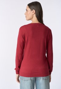 Maglione rosso lavorato a maglia con scollo rotondo, maniche lunghe e polsini a coste. Texture liscia, design aderente e senza motivi visibili.