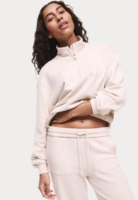 Crème-kleurige, rits-fleece sweatshirt met hoge kraag, losse pasvorm en verlaagde schouders, gecombineerd met bijpassende sweatpants met drawstring.