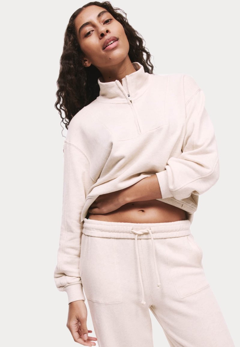 Crème-kleurige, rits-fleece sweatshirt met hoge kraag, losse pasvorm en verlaagde schouders, gecombineerd met bijpassende sweatpants met drawstring.