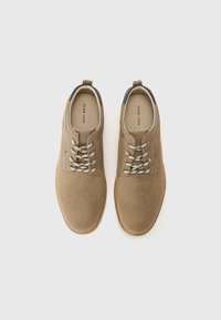 Zapatos de ante color beige con un acabado suave, que cuentan con cordones estampados, costuras claras y un talón oscuro contrastante. Suela de goma con una forma clásica.