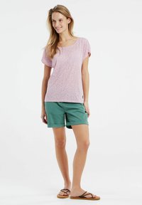 Haut rose clair à manches courtes avec un léger imprimé léopard, associé à un short vert menthe. Des sandales avec des lanières marron complètent la tenue.