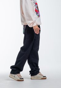 Pantalones de mezclilla negros holgados, un sudadero gráfico rosa claro con un diseño en la parte frontal y zapatillas beige con acentos oscuros.