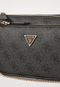 Must puidust tekstuuriga sünteetiline risti kott, millel on kuldne riistvara, kolmnurkne logo ja tõmblukkude sulg, kaunistatud sisse vajutatud mustriga.