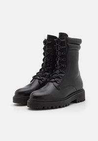 Botas de tobillo de cuero negro con puntera redondeada, cordones en la parte delantera y una robusta suela de goma con relieves. Incluye un puño acolchado para mayor comodidad.