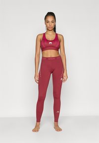 Conjunto de soutien desportivo e leggings cor bordô feitos de tecido elástico, com um logótipo no peito e na perna, e uma cintura alta para suporte.