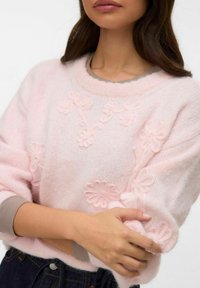 Jasnoróżowy, dziany sweter z teksturowaną, kwiatową haftowaną dekoracją. Posiada prążkowany kołnierz i mankiety, z miękkim, puszystym wyglądem.