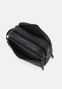 Black leather crossbody bag with multiple zippered compartments, flat structure, smooth texture, and silver-tone hardware accents.