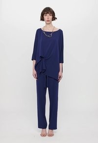 Navy blue two-piece outfit featuring a loose-fitting top with a knotted detail at the waist and straight-leg pants. Smooth fabric texture.