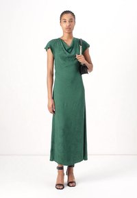 Cowl neck, fitted green dress with short flutter sleeves, falling to mid-calf. Paired with black handbag and strappy heels. Smooth texture.