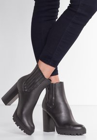 Czarne skórzane botki za kostkę na wysokim słupku, z elastycznymi panelami bocznymi i teksturowaną podeszwą. Charakteryzujące się eleganckim, gładkim wykończeniem.