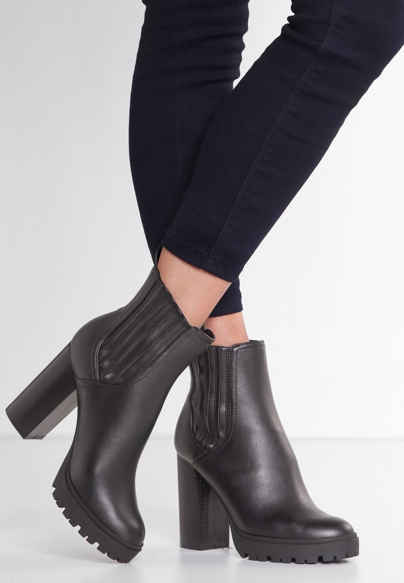 Czarne skórzane botki za kostkę na wysokim słupku, z elastycznymi panelami bocznymi i teksturowaną podeszwą. Charakteryzujące się eleganckim, gładkim wykończeniem.