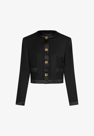 Melna īsa jaka ar garām piedurknēm, kurai ir spoži zelta pogas, divas priekšējās kabatas un satīna apdare apkaklē un piedurkņos.