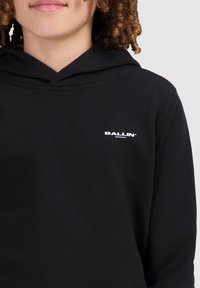 Zwarte hoodie van katoen met een voorzak. Kenmerkt zich door een witte "BALLIN" logo op de borst en een ontspannen pasvorm. Gladde textuur.