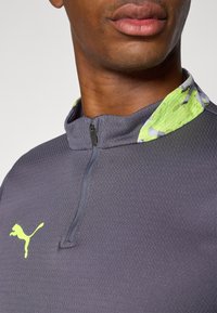 Grey athletic shirt with a half-zip collar; features a textured surface and a contrasting vibrant green and patterned collar trim.