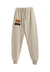 Pantalones de chándal beige con cintura elástica, que cuentan con un parche de oso texturizado en el bolsillo izquierdo y un acento de etiqueta negra encima de este.