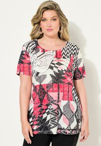 Camiseta gráfica con patrones abstractos en rojo, negro y blanco, de manga corta y cuello redondo. Tejido suave y texturizado.