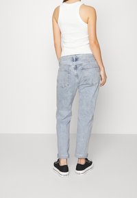 Vaaleansiniset farkut, joissa on rento sovitus, käännetyt lahkeet ja takataskut. Yhdistetty valkoiseen ilmanhihoiseen tanktoppiin ja mustiin lenkkareihin.