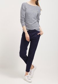Chino slim fit blu navy abbinati a una maglietta a maniche lunghe grigio e bianco a righe. Sneakers bianche con tre cinturini regolabili.