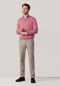 Pullover rosa chiaro con zip a quarto, abbinato a chinos beige e scarpe scure. Il maglione presenta una texture liscia e un design classico.