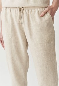 Linen hlače na vezanje u svijetloj bež boji. Imaju elastični pojas, bočne džepove i teksturiranu tkaninu s suptilnim uzorkom.