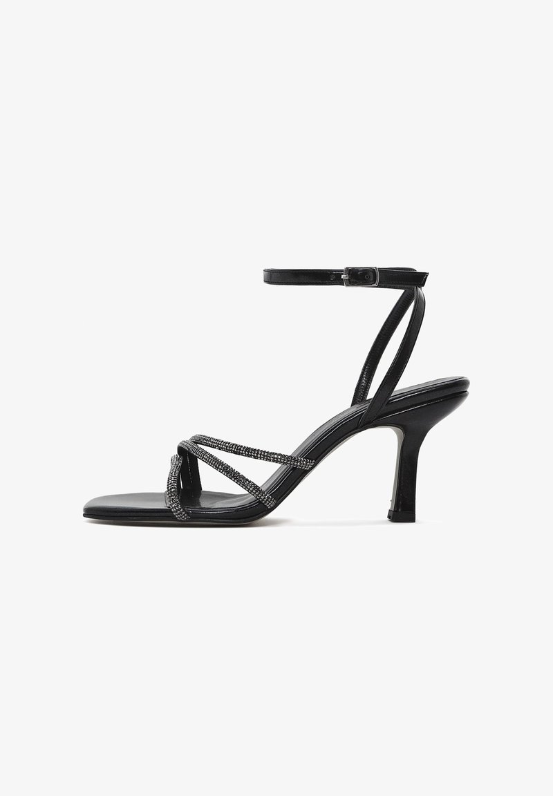 Sandal à talons hauts noirs avec un design ouvert à l'avant, ornée de brides entrecroisées décorées de petites perles et d'une sangle de cheville réglable.