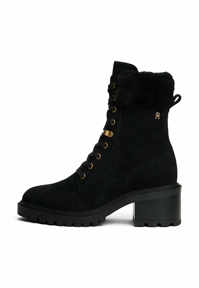 Bottines en daim noir avec un col en fourrure, matériel doré, devant lacé et semelle en caoutchouc noire robuste. Elles comportent un talon carré.