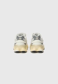 Sneaker bianchi e grigi con una suola gialla spessa, caratterizzati da una tomaia liscia, una forma arrotondata e dettagli testurizzati sul tallone.