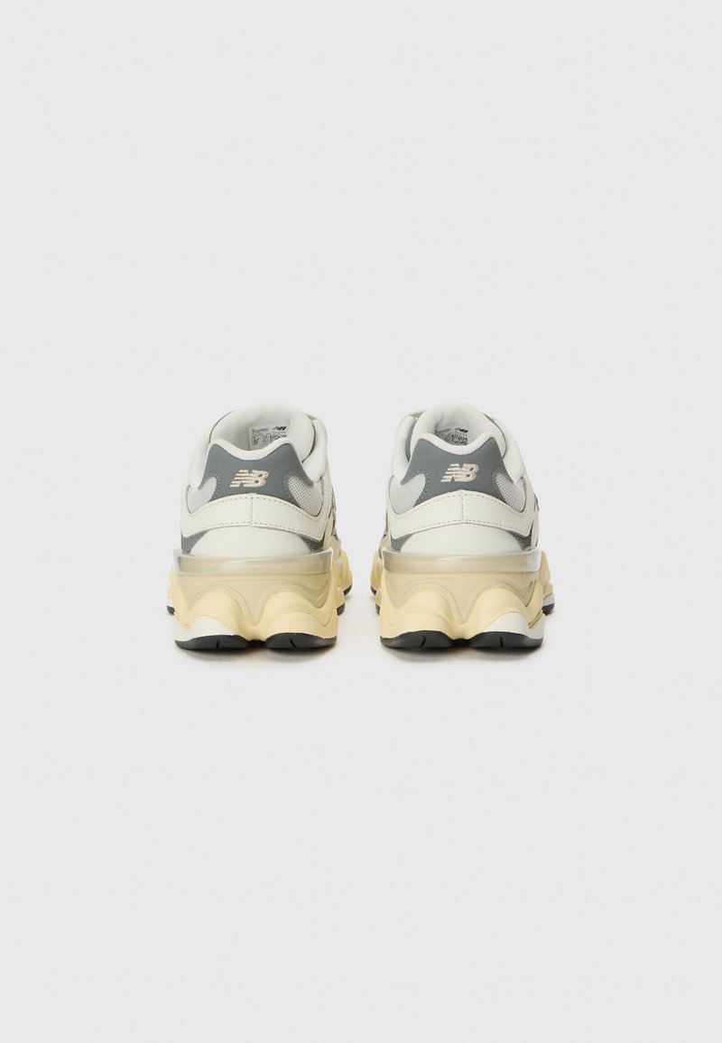 Sneaker bianchi e grigi con una suola gialla spessa, caratterizzati da una tomaia liscia, una forma arrotondata e dettagli testurizzati sul tallone.