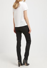Černé slim-fit kalhoty spárované s hladkým bílým tričkem. Mezi významné detaily patří černé vysoké podpatky se zlatými akcenty.