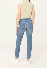 Džíny z modrého denimu s vysokým pasem, slim fit a pěti kapsami, s mírným bělením a kontrastním šitím. Nohou bílých tenisek.